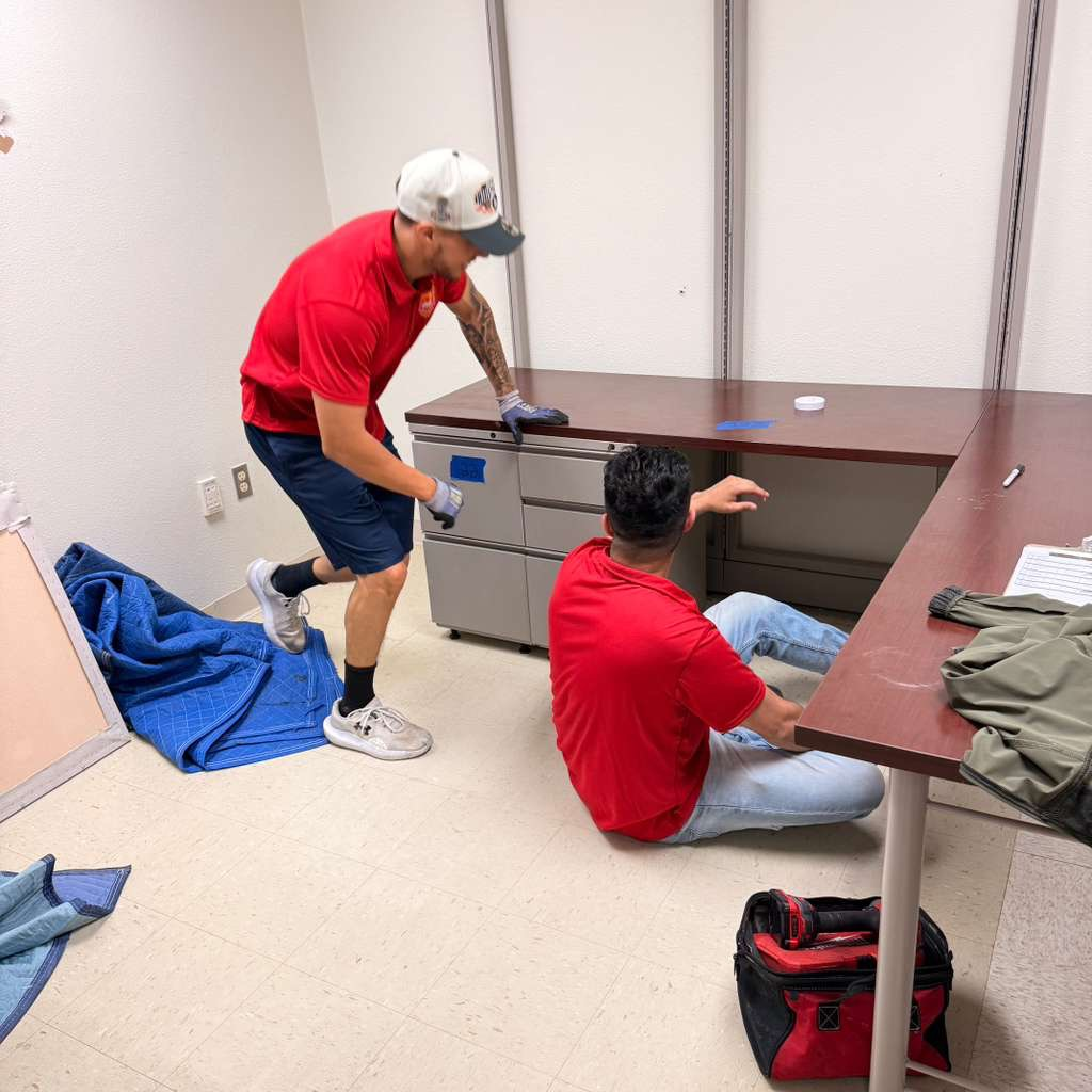 Two individuals in red shirts working in an office, one sitting on the floor.