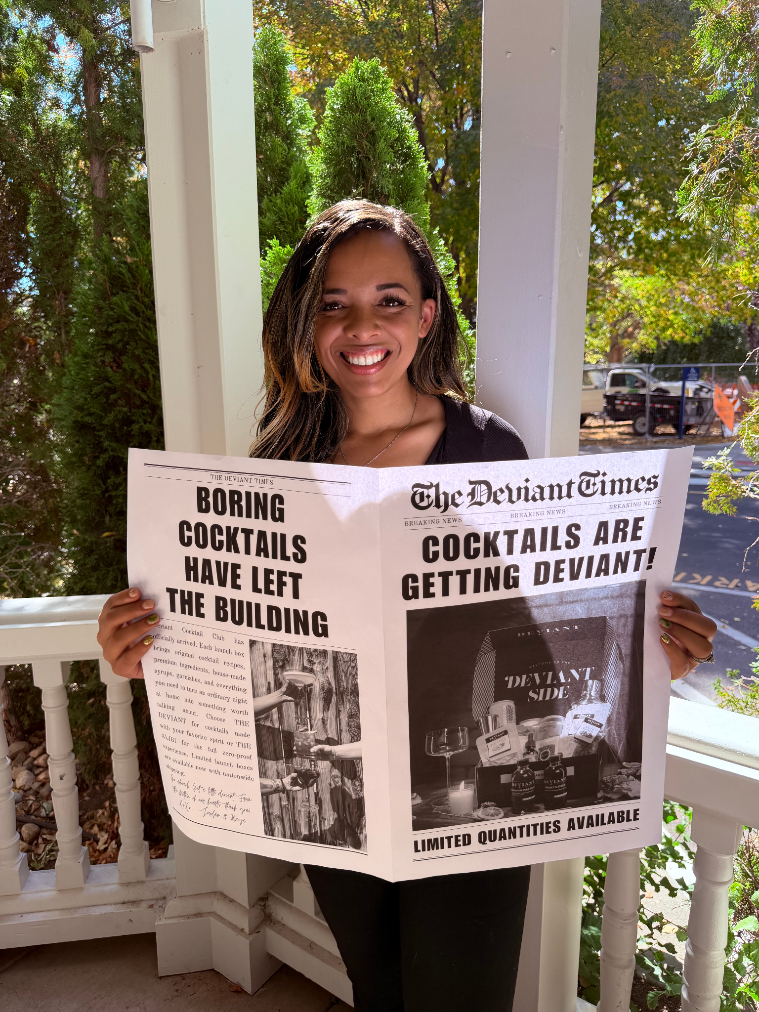 Smiling woman holding a large newspaper titled "The Deviant Times" outdoors