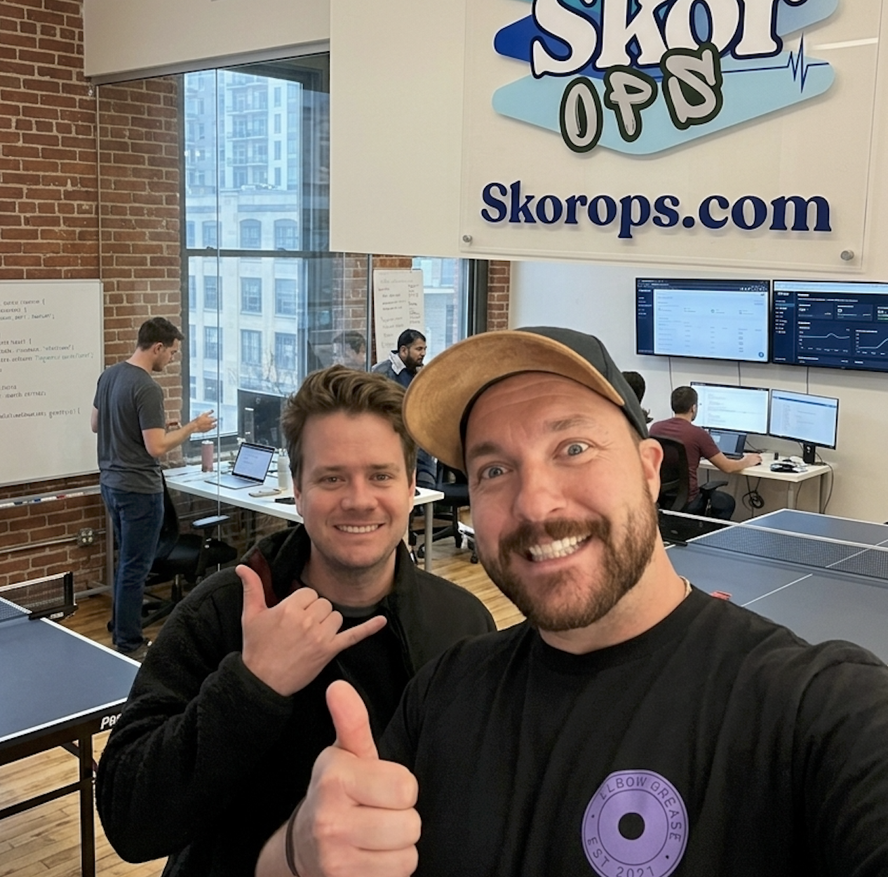 Two men posing for a selfie in an office with ping pong tables and screens
