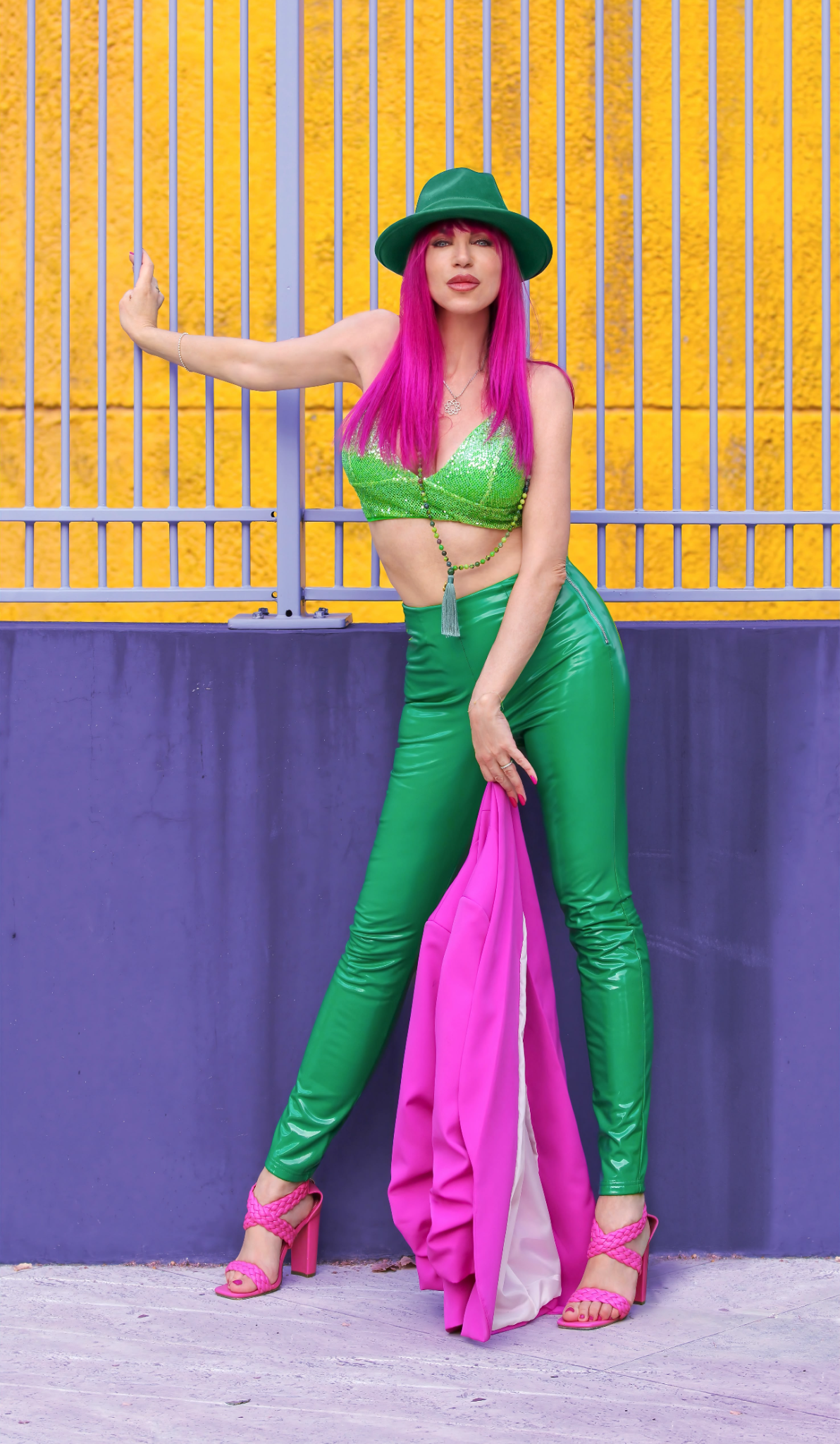 A woman with pink hair poses in a green outfit against a colorful backdrop