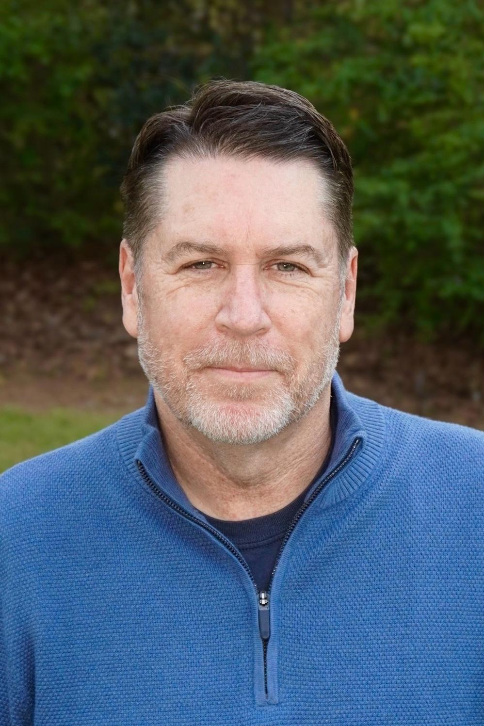 Middle-aged man with short hair and a beard, wearing a blue sweater outdoors