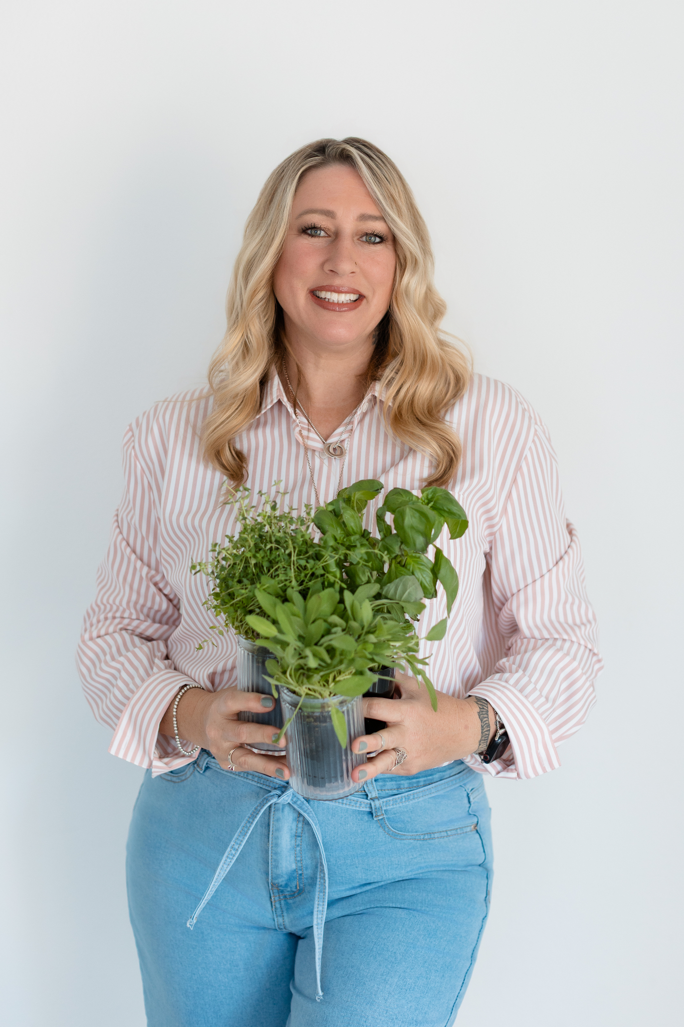 A woman in a striped shirt holds a pot of fresh herbs.
