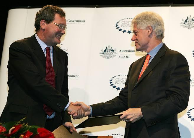 Two men shake hands while signing an agreement at a formal event