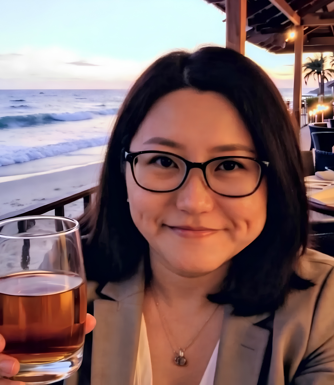 Person holding a drink, smiling by the seaside during sunset