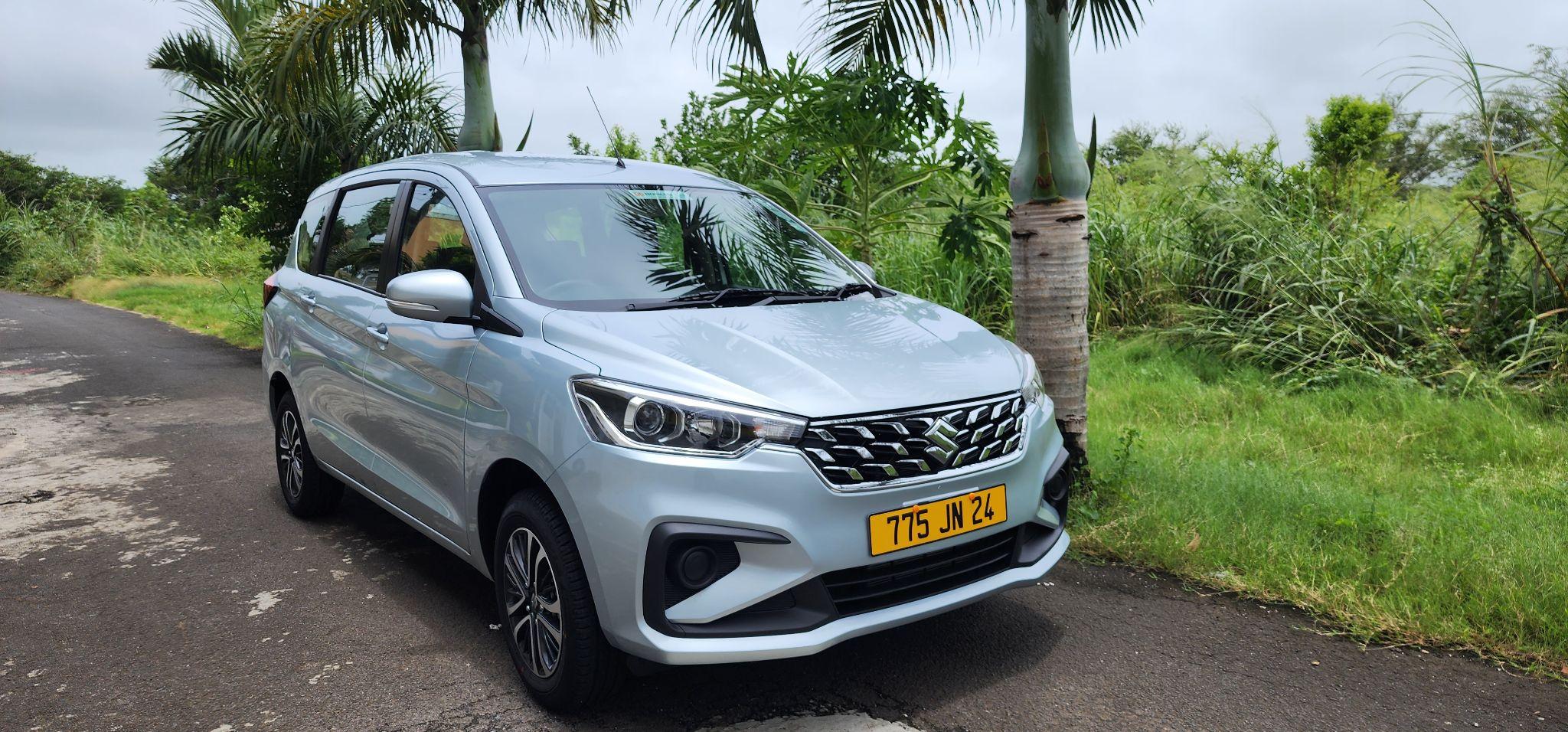 A silver car parked on a road surrounded by greenery and palm trees