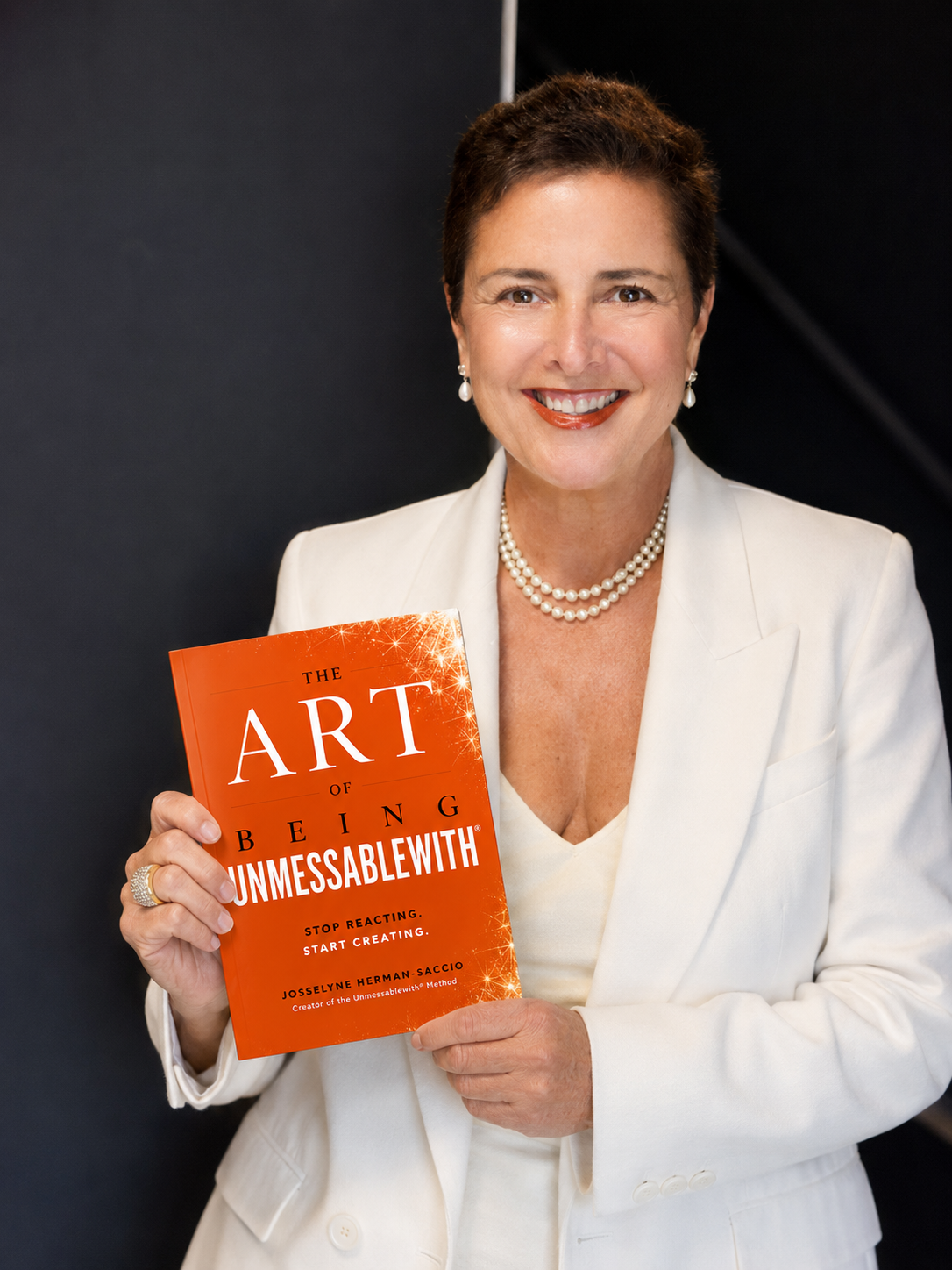 A woman in a white suit holds a book titled "The Art of Being Unmessablewith"