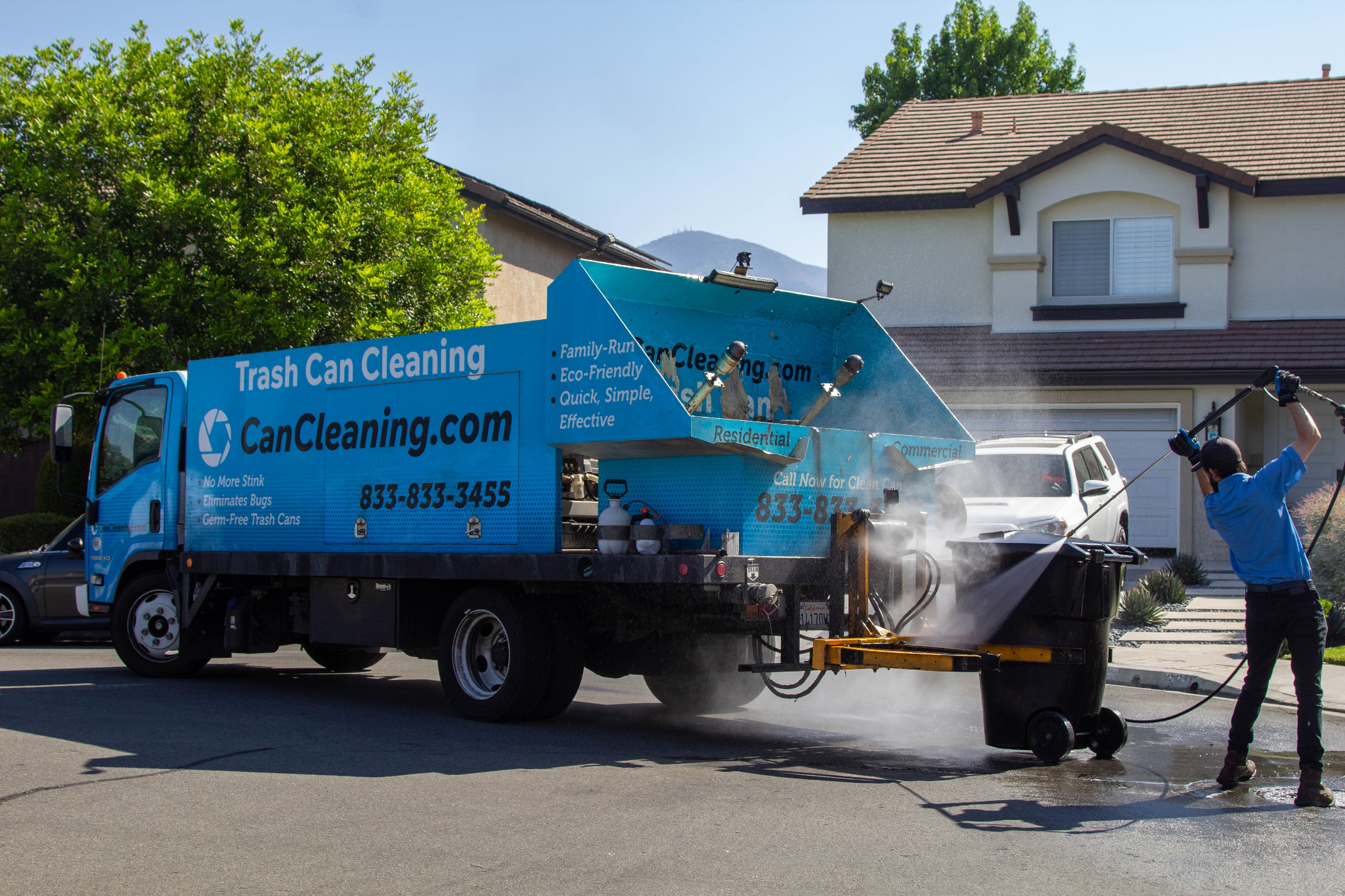 A truck with a trash can cleaning system operating on a residential street