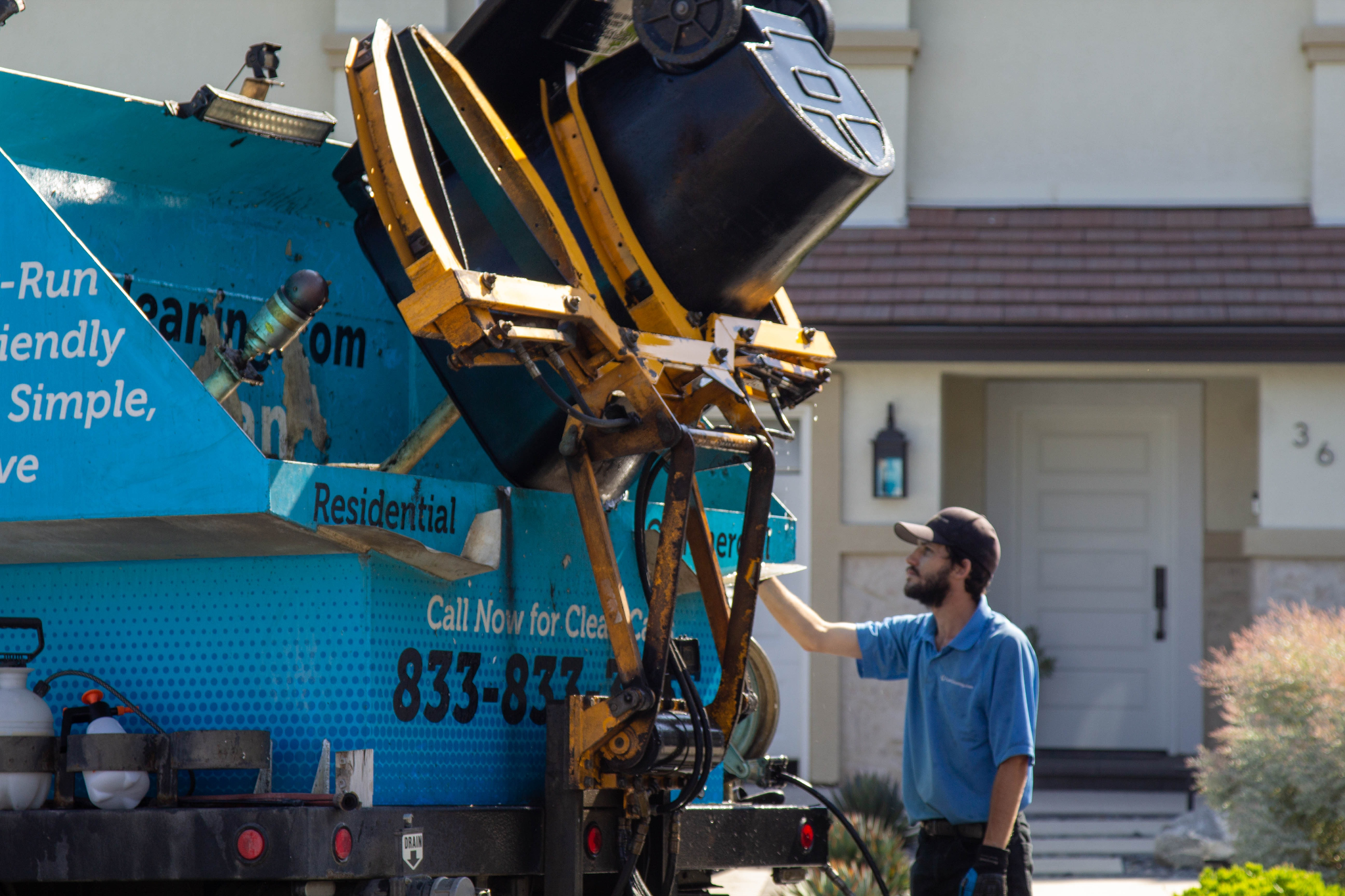 A worker operates a blue waste collection truck outside a residential building