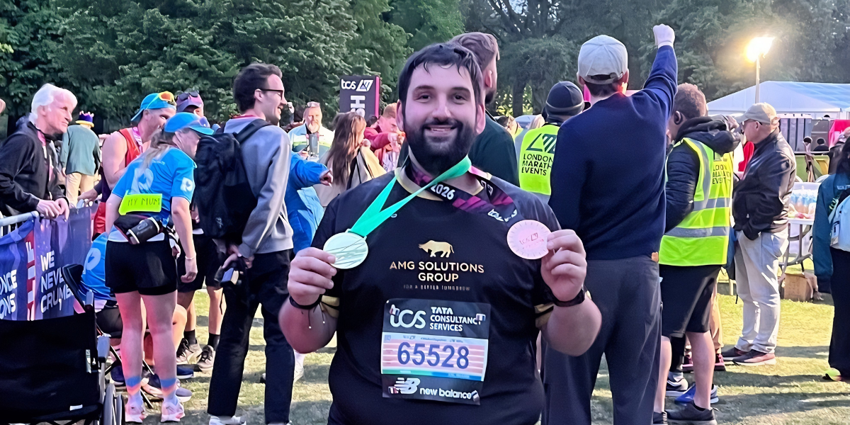 A man holds medals after finishing a marathon, surrounded by other participants and spectators.