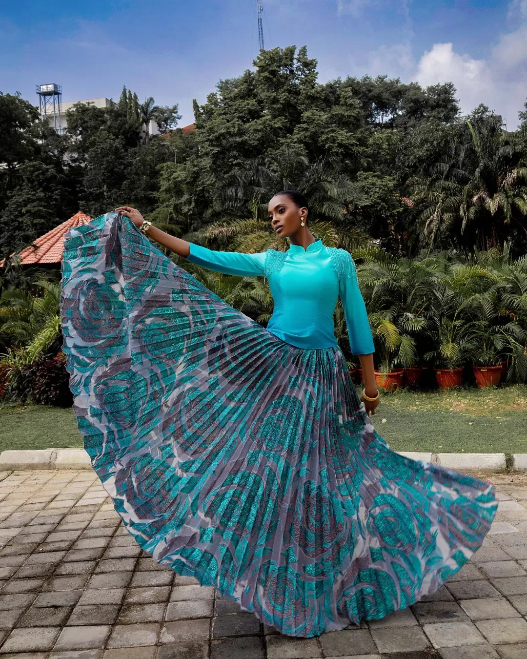 A model in a turquoise outfit gracefully poses with a flowing patterned skirt outdoors
