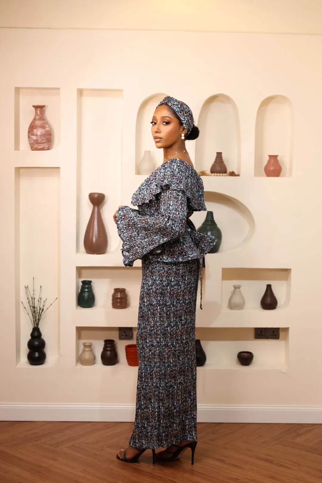 A woman in a patterned outfit poses against a decorated wall display.