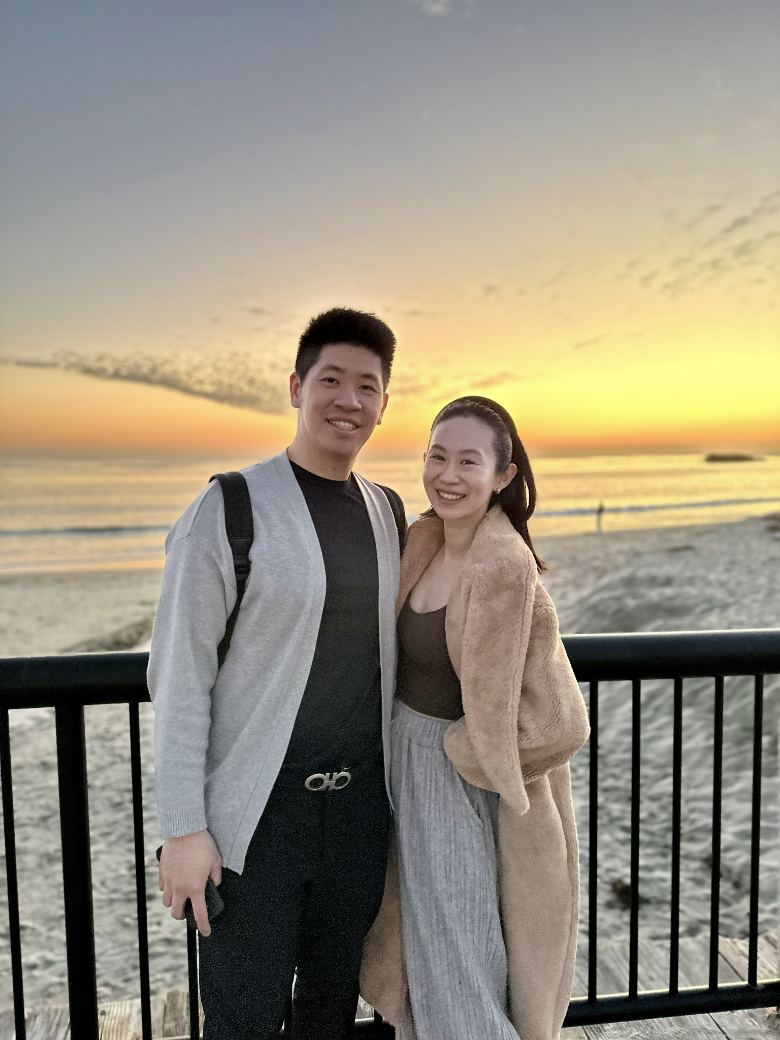 A couple poses together on a beach during sunset with vibrant colors in the sky