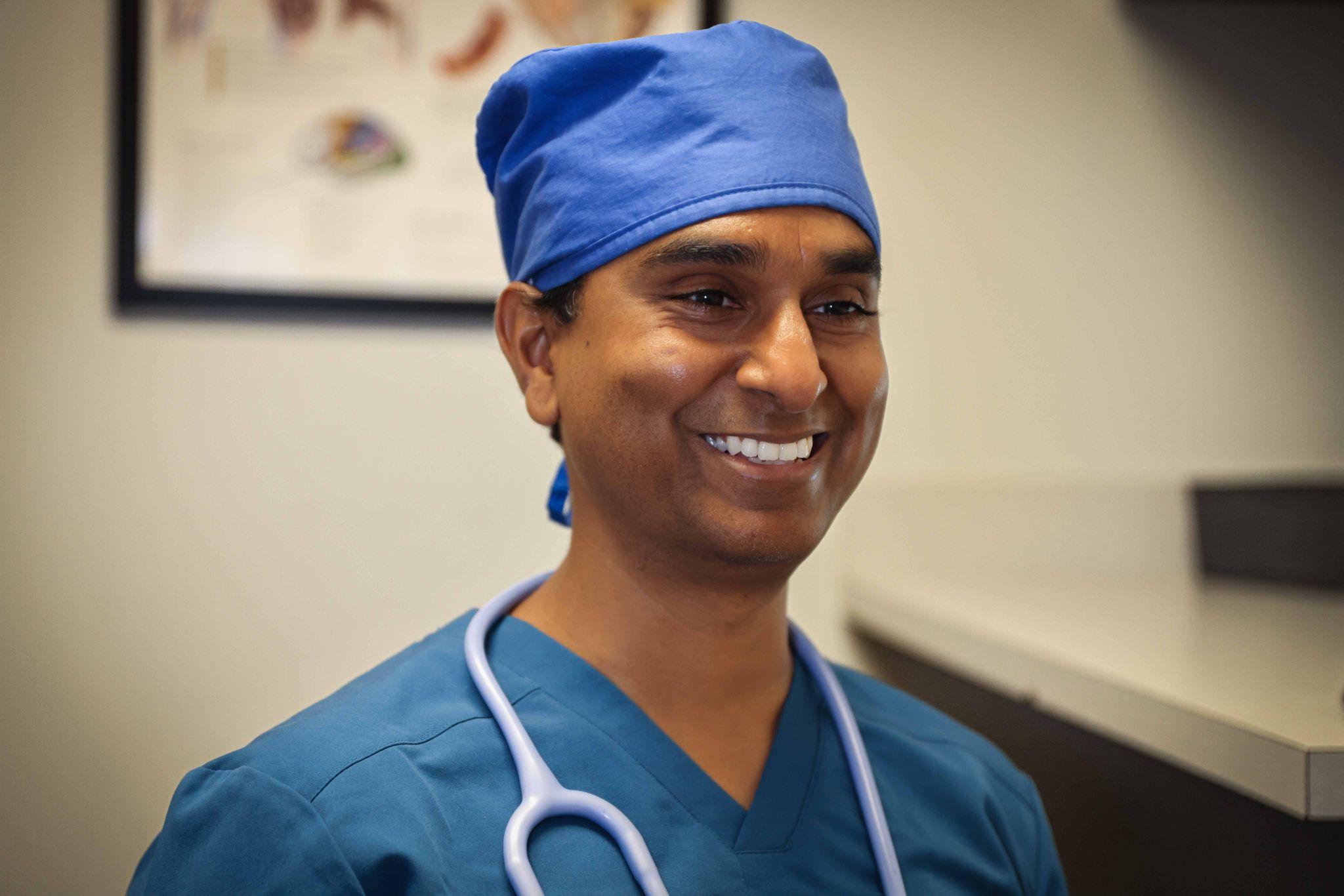 Smiling medical professional in scrubs and a blue surgical cap with a stethoscope