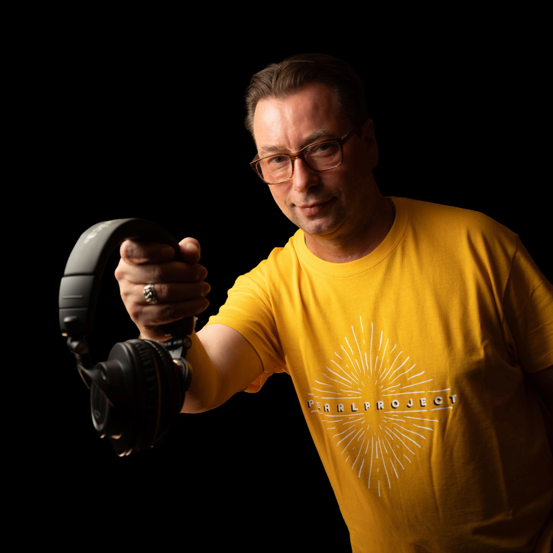 Man in a yellow shirt holding headphones, posing against a black background