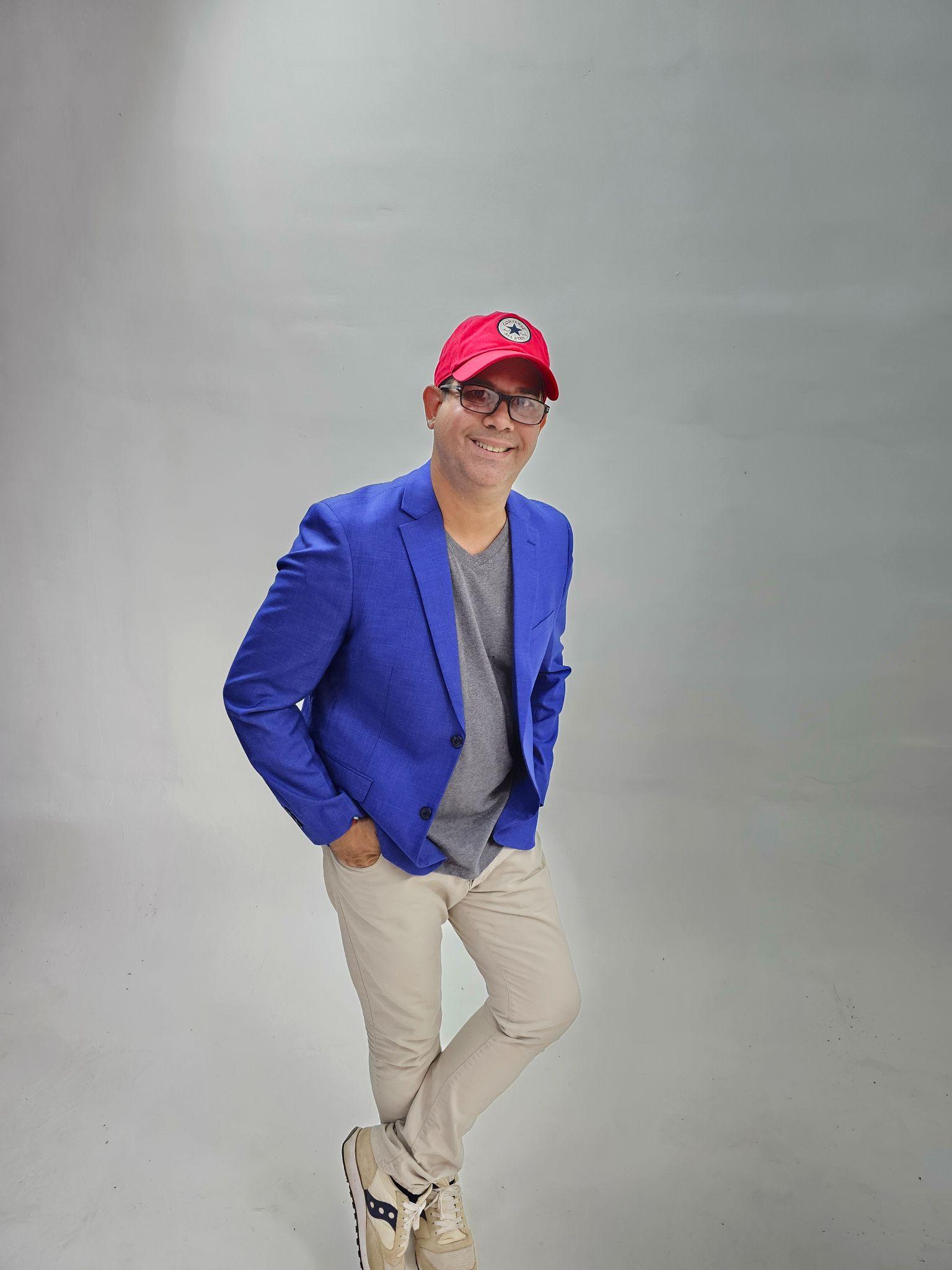 Man in a blue blazer and red cap posing against a gray background