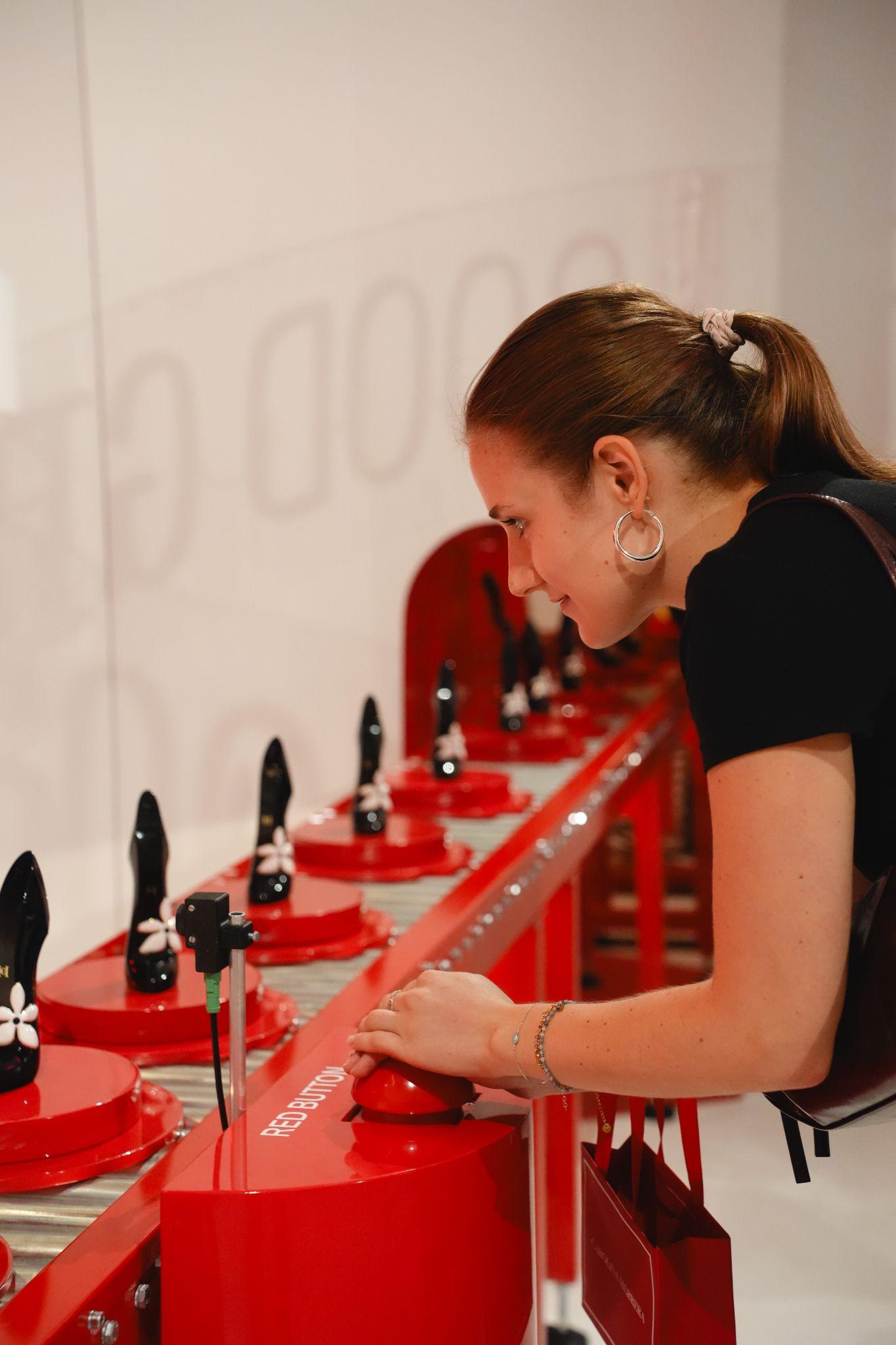 A young woman examines a display of red high-heeled shoes.