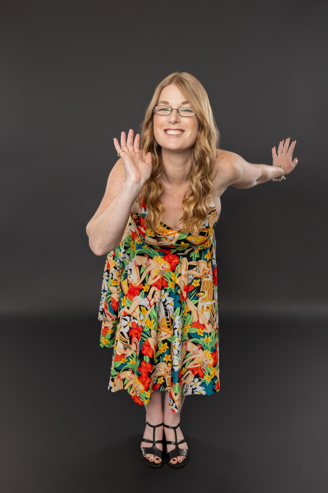 A smiling woman in a colorful floral dress posing playfully against a dark background