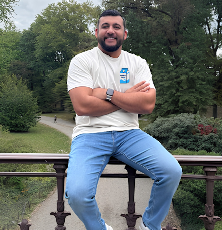 Man sitting on a railing in a park, wearing a white shirt and jeans