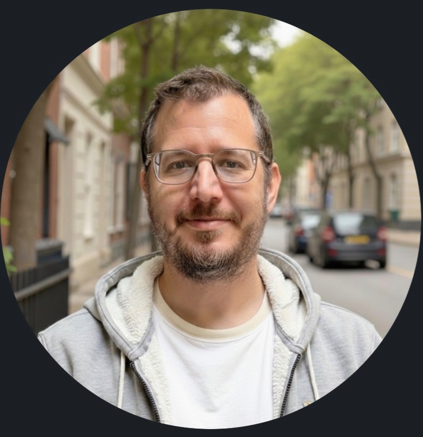 Man with glasses and a beard stands on a street lined with trees