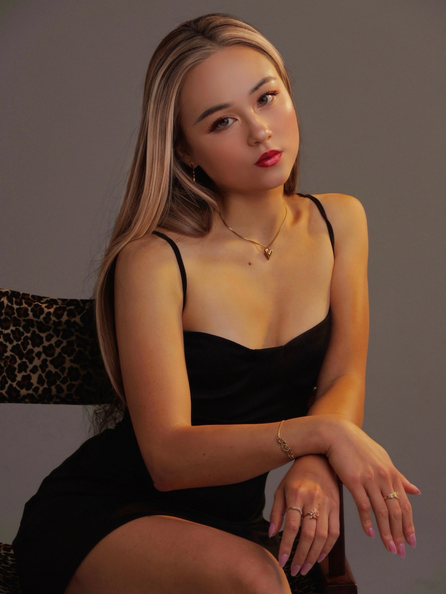 A young woman in a black dress poses elegantly with long hair and jewelry