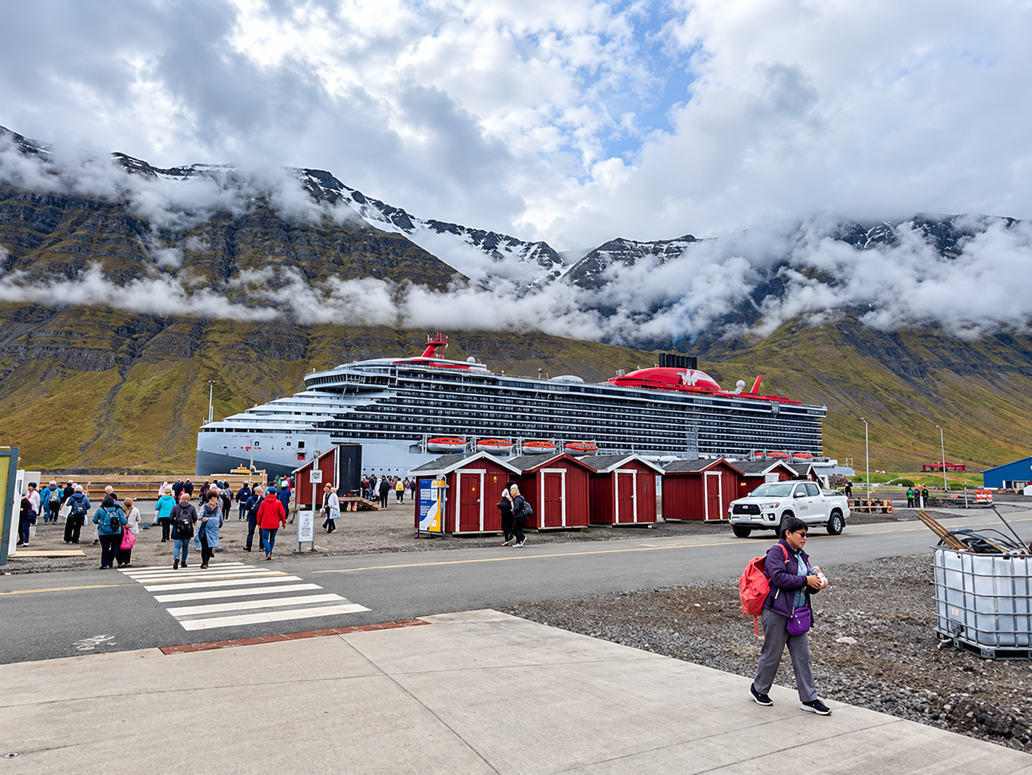Cruise ship docked near red cabins with mountains and clouds in the background
