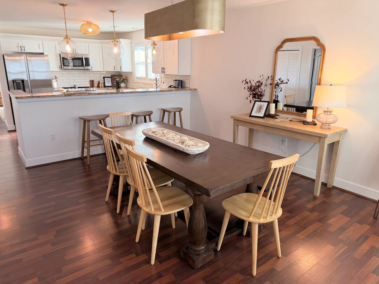 Bright dining area with a wooden table, chairs, and connected kitchen in the background