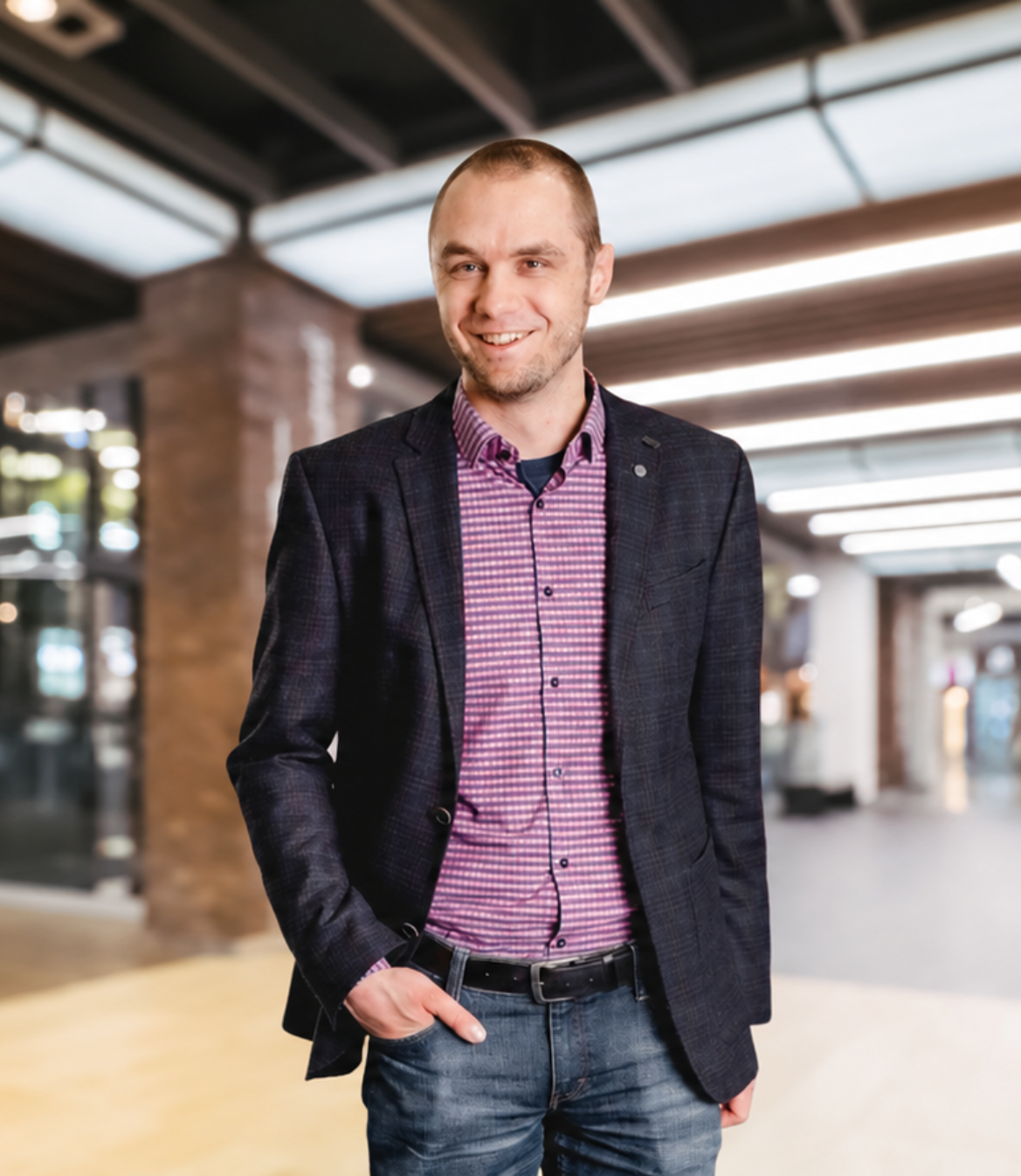 Smiling man in a blazer and checkered shirt standing in a modern interior setting