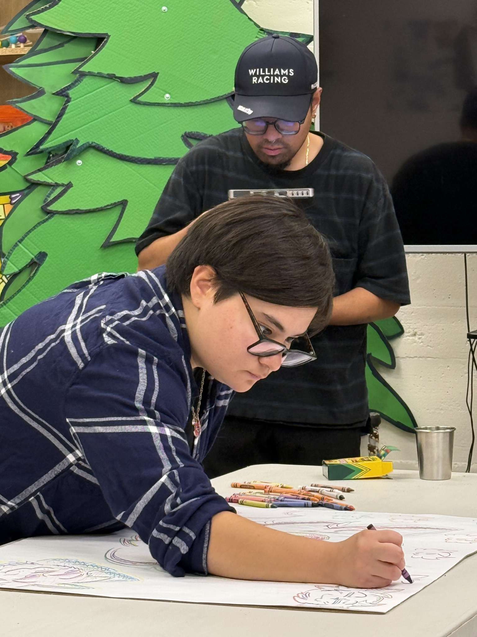 A woman colors on paper while a man takes notes in the background