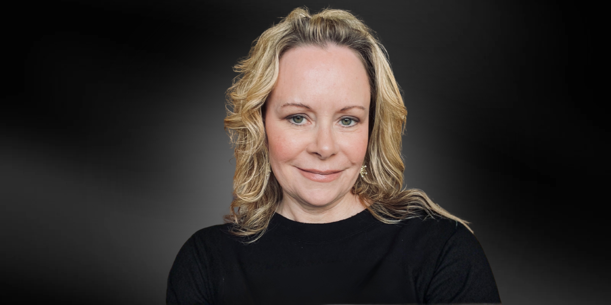 A smiling woman with blonde hair wearing a black shirt against a dark background