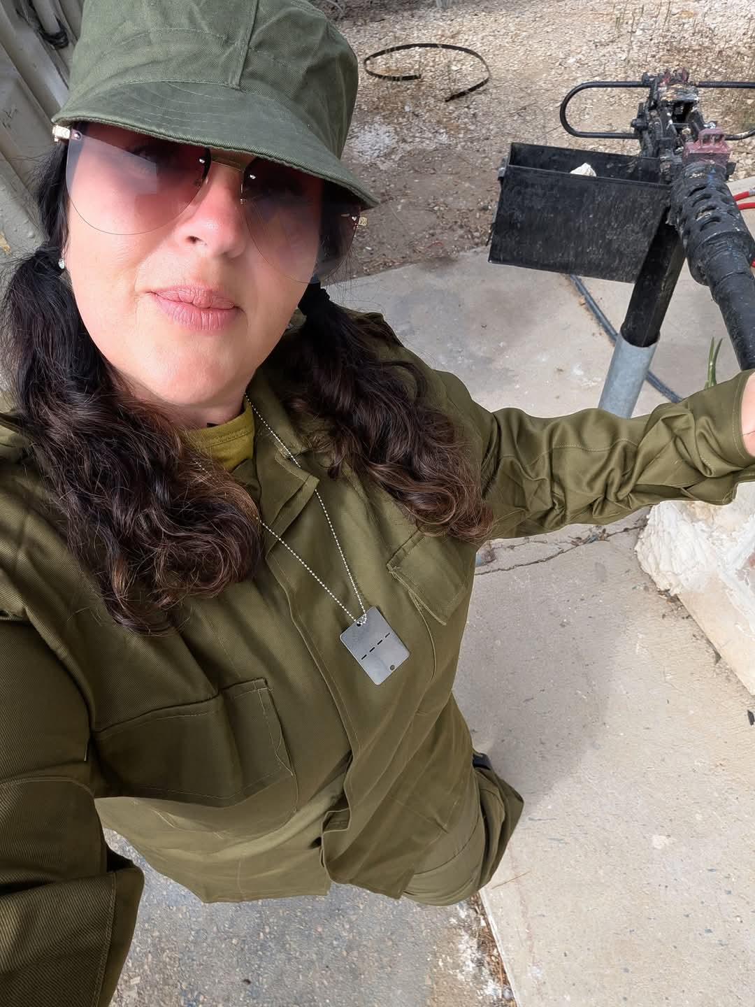 Woman in military-style uniform and cap posing near a weapon on display