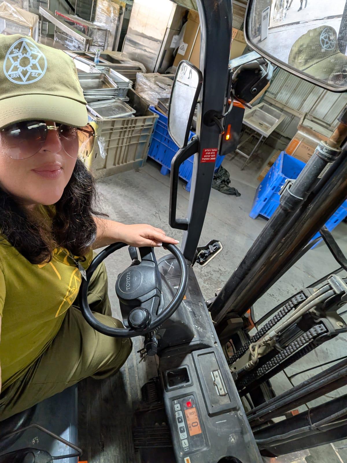Person sitting in a forklift inside a warehouse, wearing a cap and sunglasses