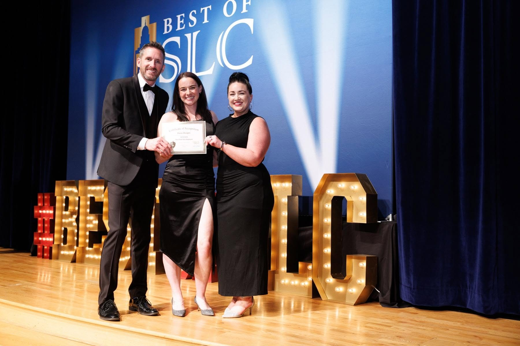 Three people pose with an award on stage at a ceremony with lights.