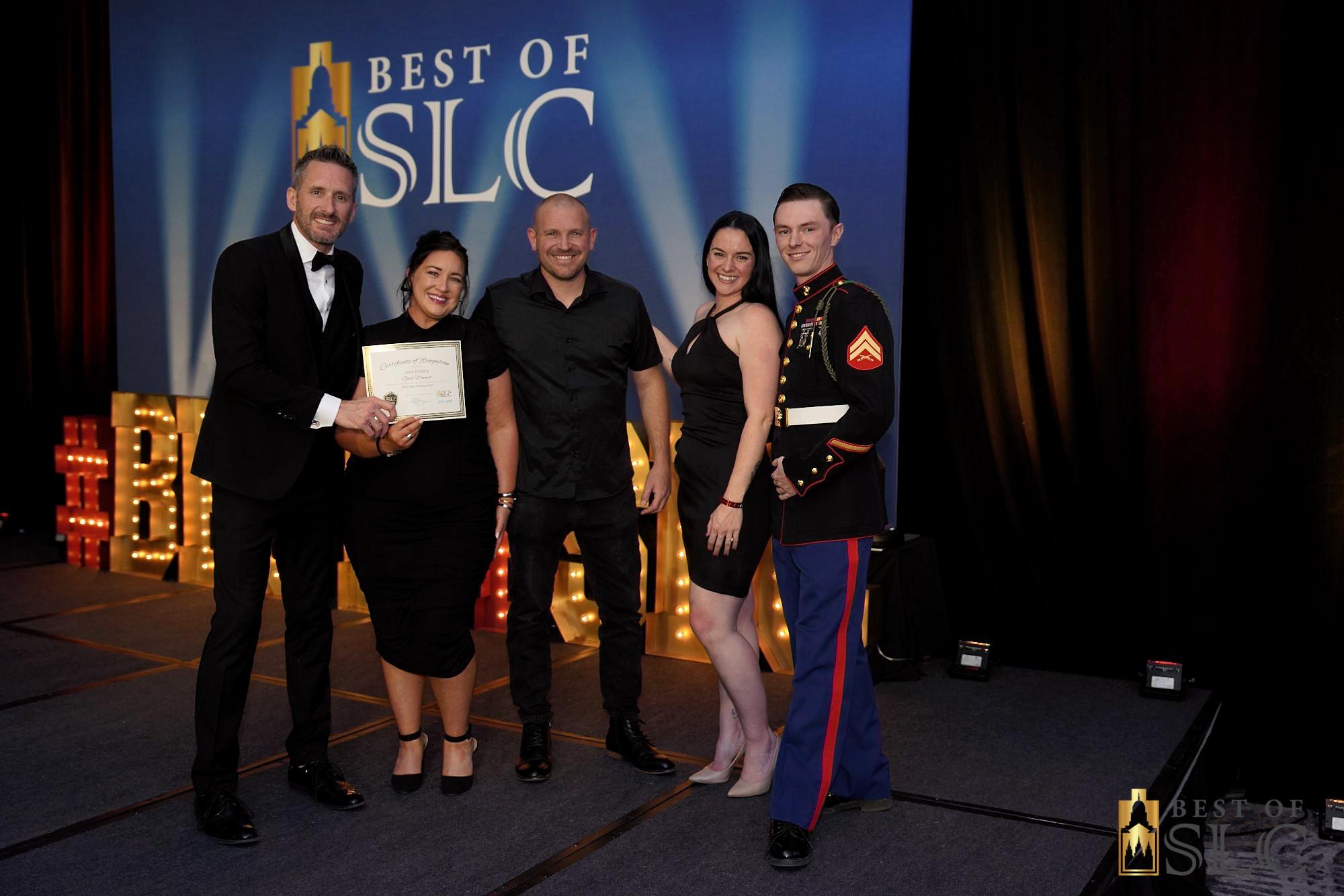 Five individuals pose together on stage at an award ceremony holding a certificate