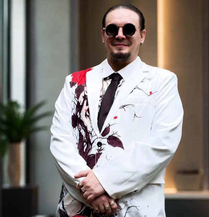 Man in stylish white suit with floral design and sunglasses standing confidently indoors