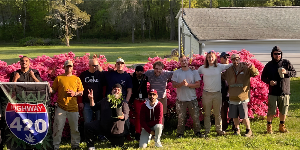 Group of people posing outdoors in front of blooming pink flowers holding plants and banners