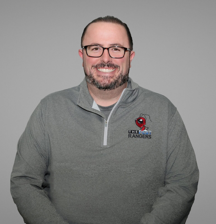 Smiling man in a gray sweater, standing against a gray background.