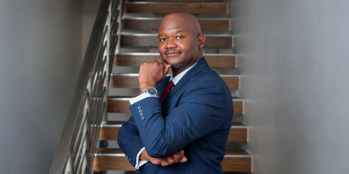 Man in a suit poses confidently on a staircase, resting chin on hand