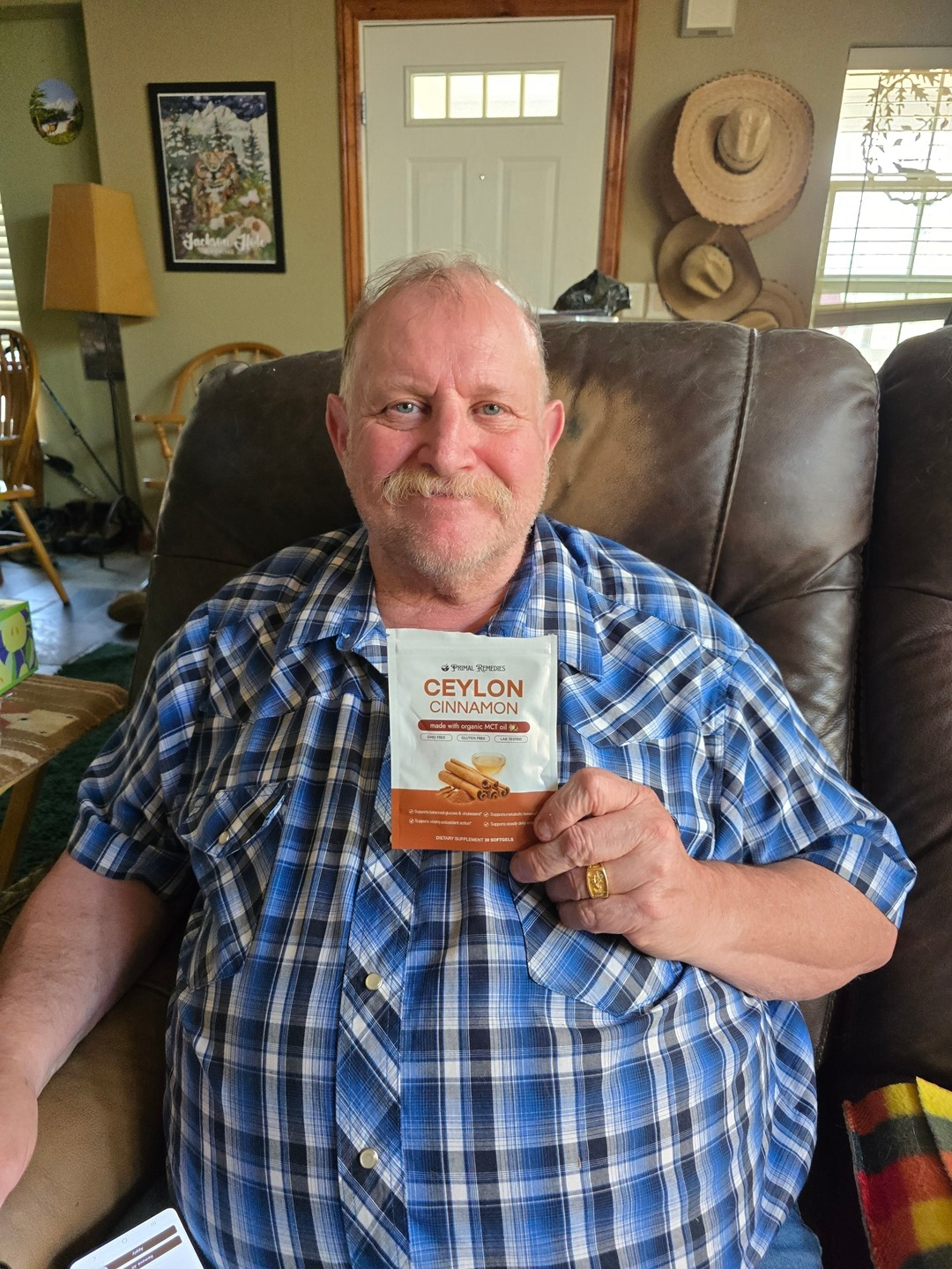 Man sitting in a chair holding a packet of Ceylon cinnamon, smiling.