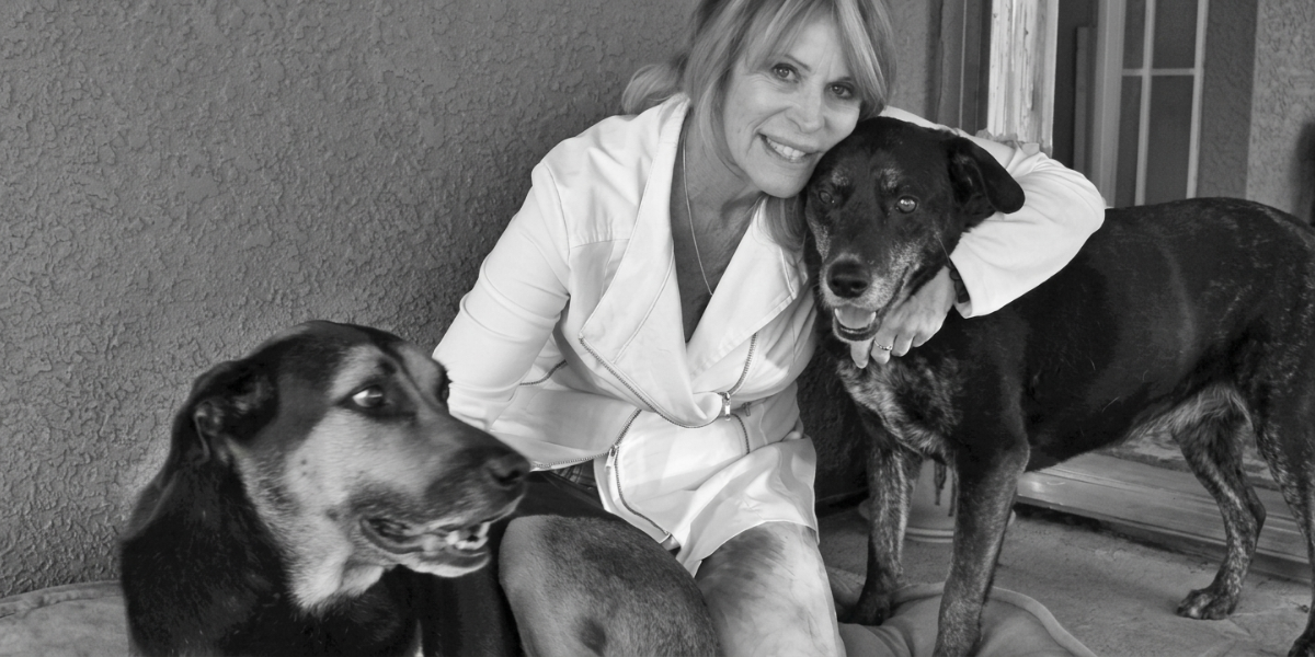 Woman in a white coat sitting with two dogs on a soft surface