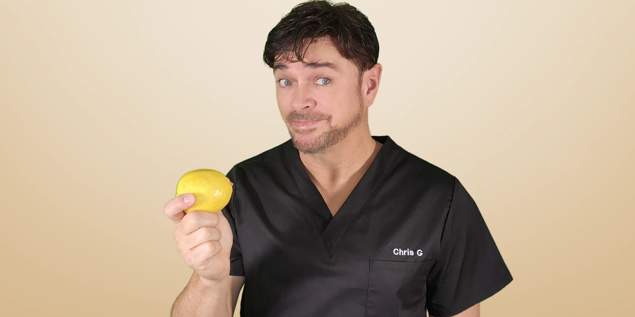 Man in black scrubs holding a yellow lemon with a playful expression