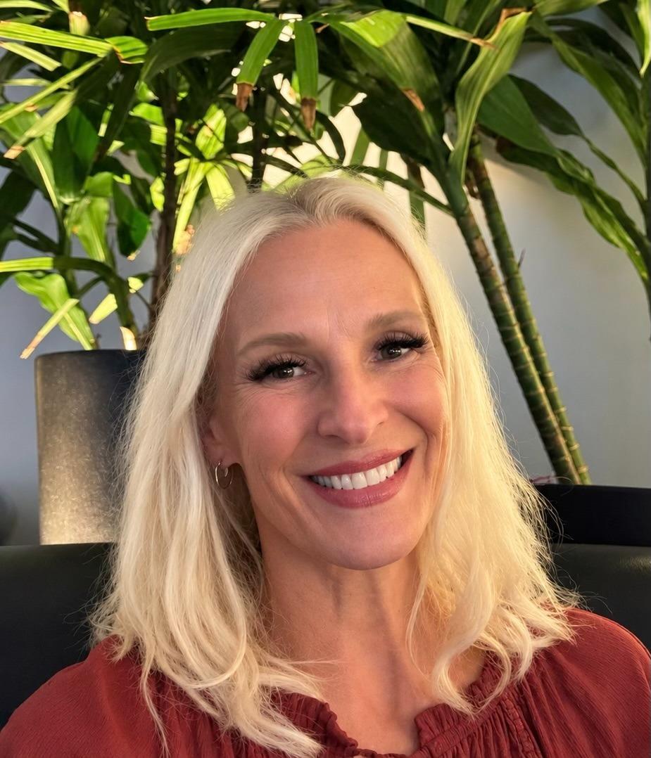 Smiling woman with long blonde hair sitting in front of green plants