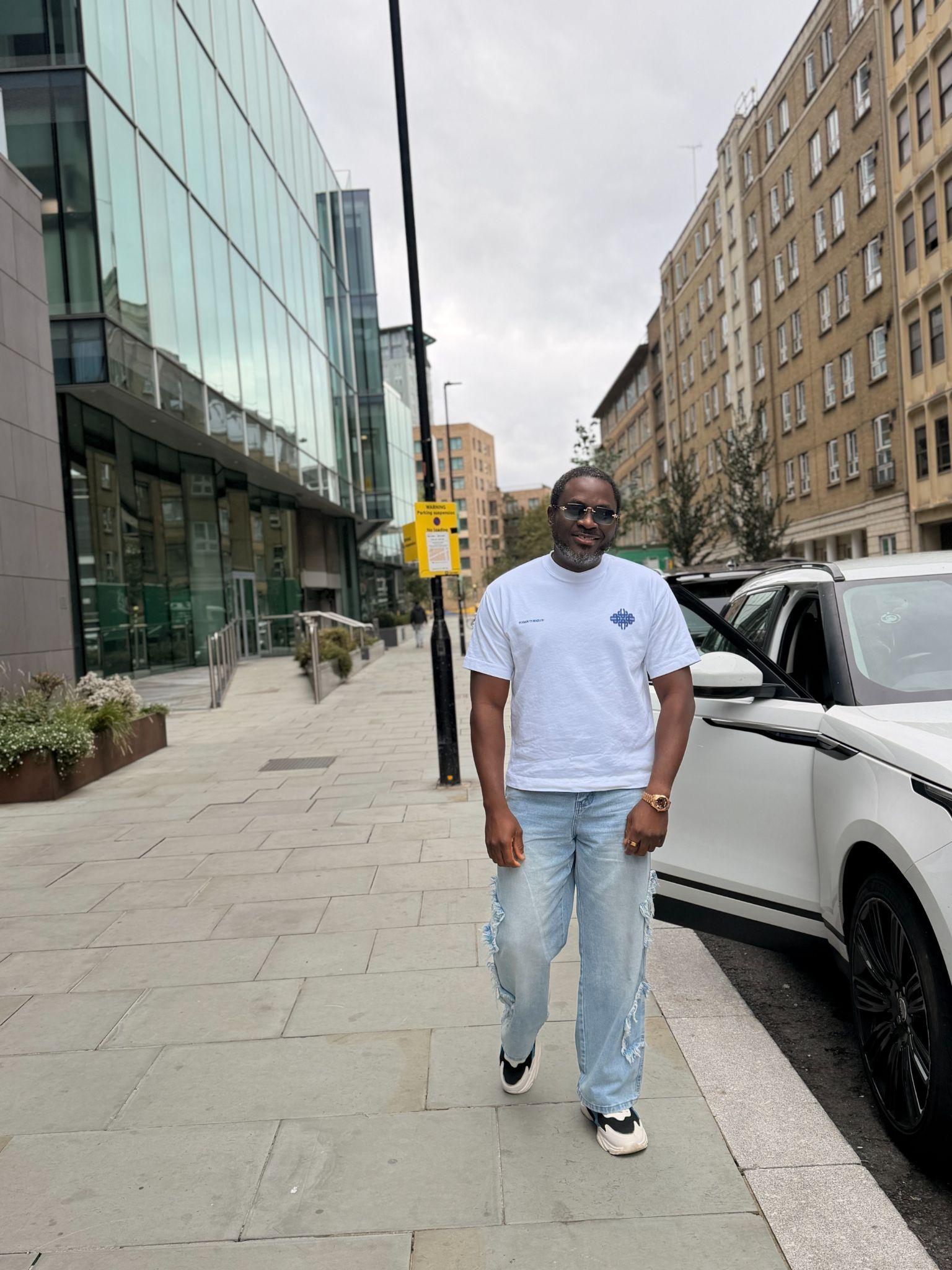 A man in casual attire walks near a modern building and a car.