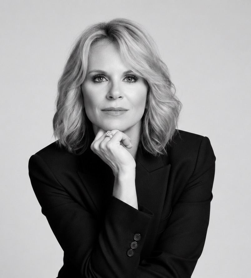 A woman with wavy blonde hair poses thoughtfully in a black blazer.