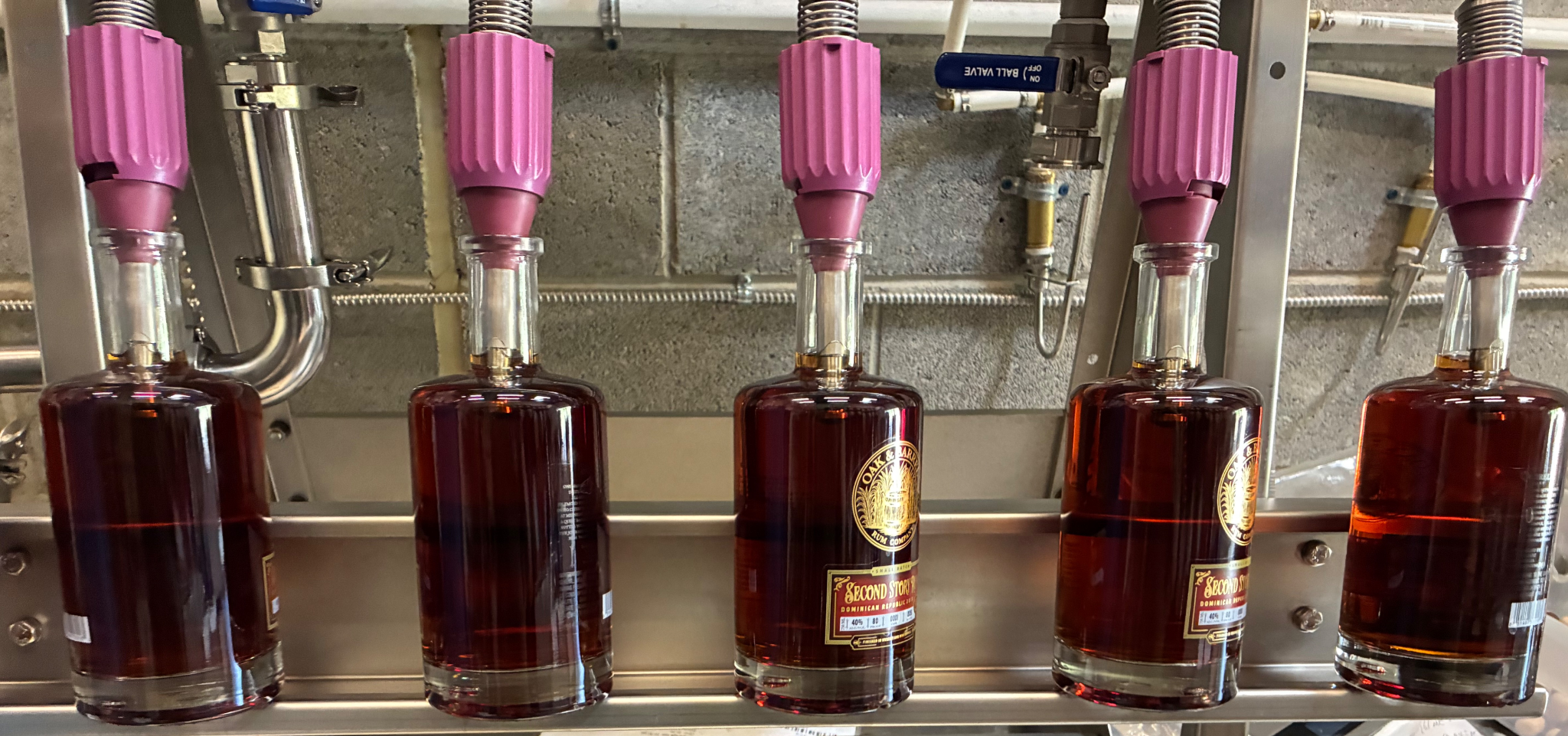 Bottles of brown liquid being filled on a production line with purple nozzles