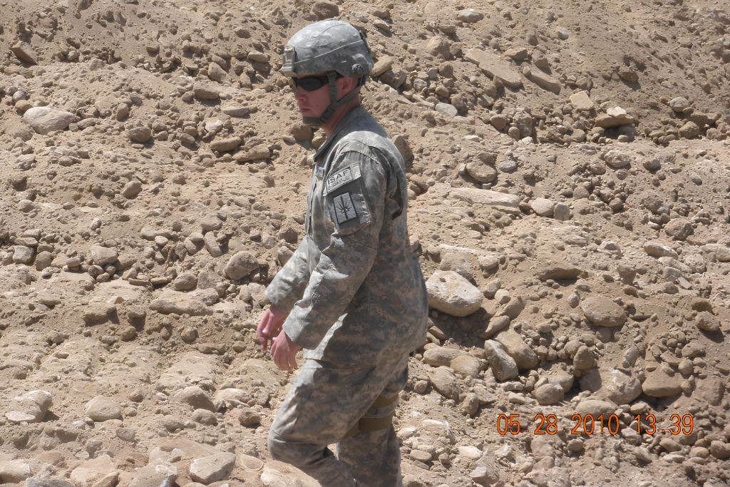 Soldier in military uniform navigating rocky terrain under bright sunlight