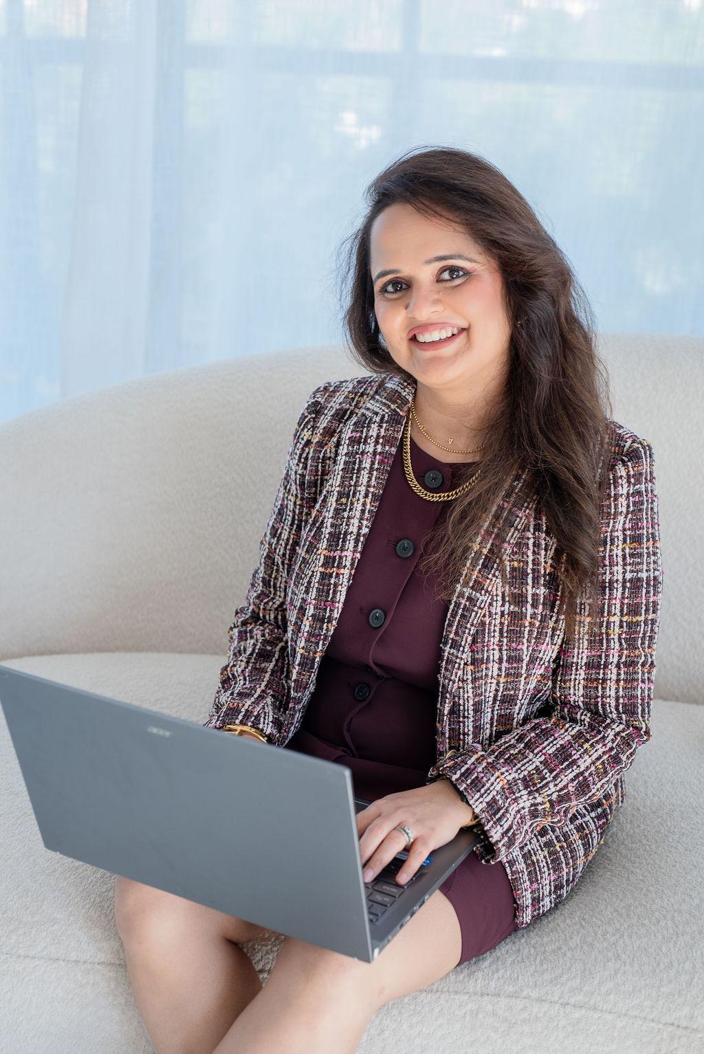 Woman in a stylish outfit working on a laptop while sitting on a sofa