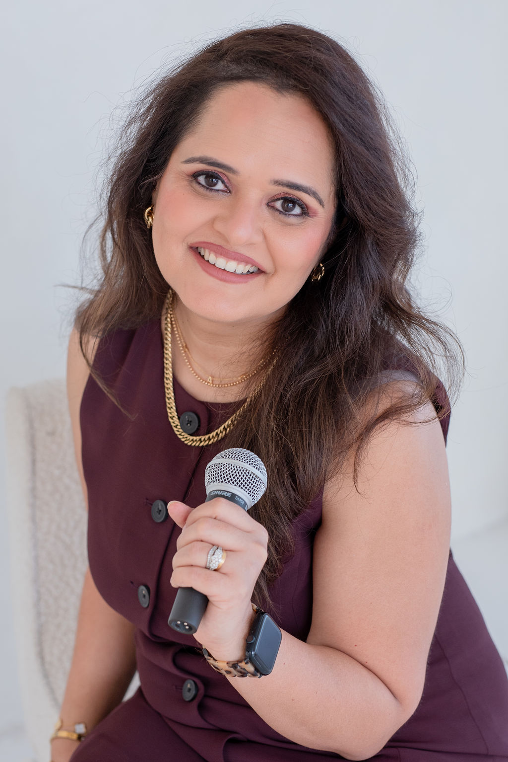 Smiling woman holding a microphone, wearing a purple dress and gold jewelry