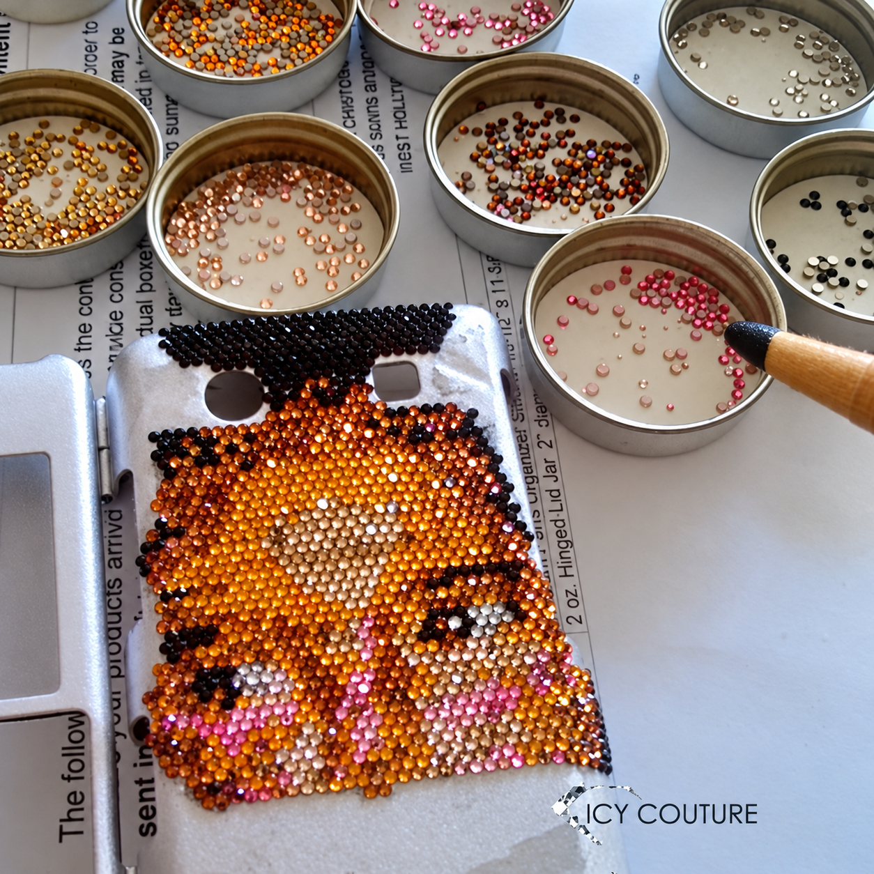 A crafting setup with a rhinestone phone case design and arranged colorful rhinestones
