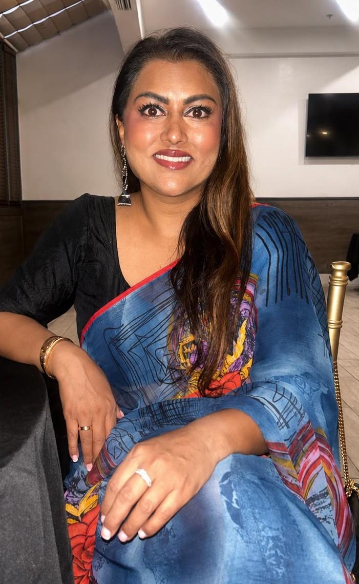 A woman in a colorful saree, seated with a warm smile at an event