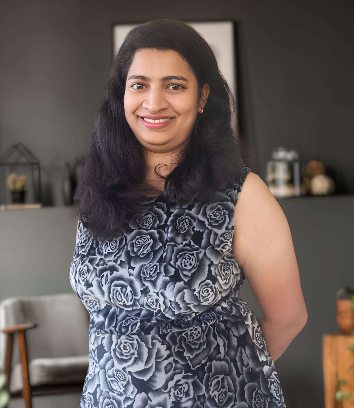 Smiling woman in a floral dress stands against a modern, softly lit background.
